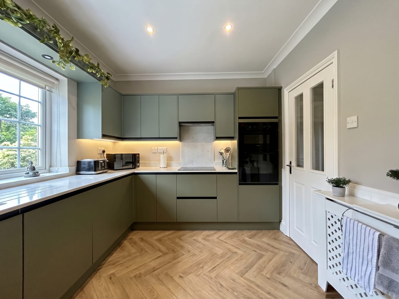 The same kitchen reimagined in modern sage green with a herringbone floor